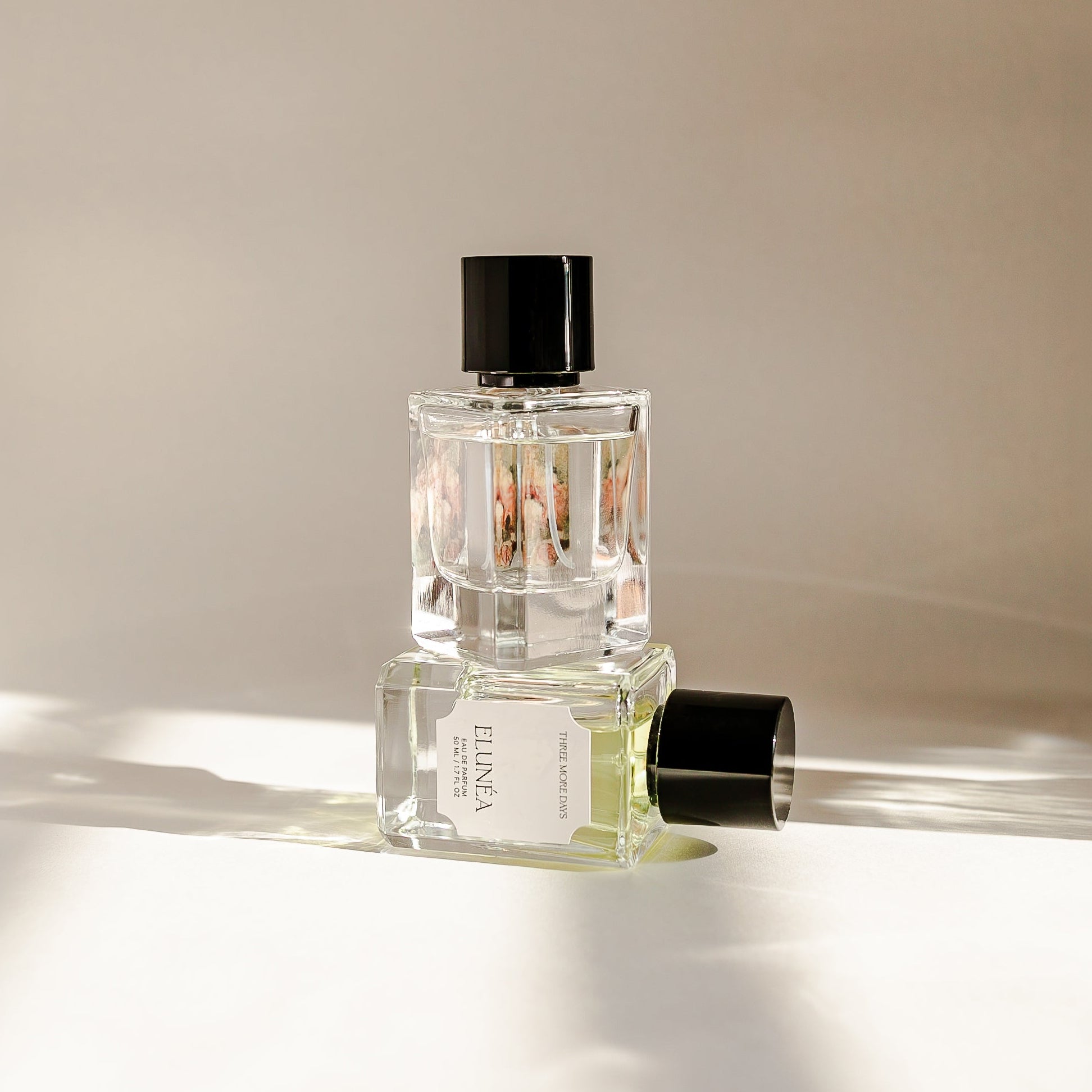 Two perfume bottles on a reflective surface with a neutral background