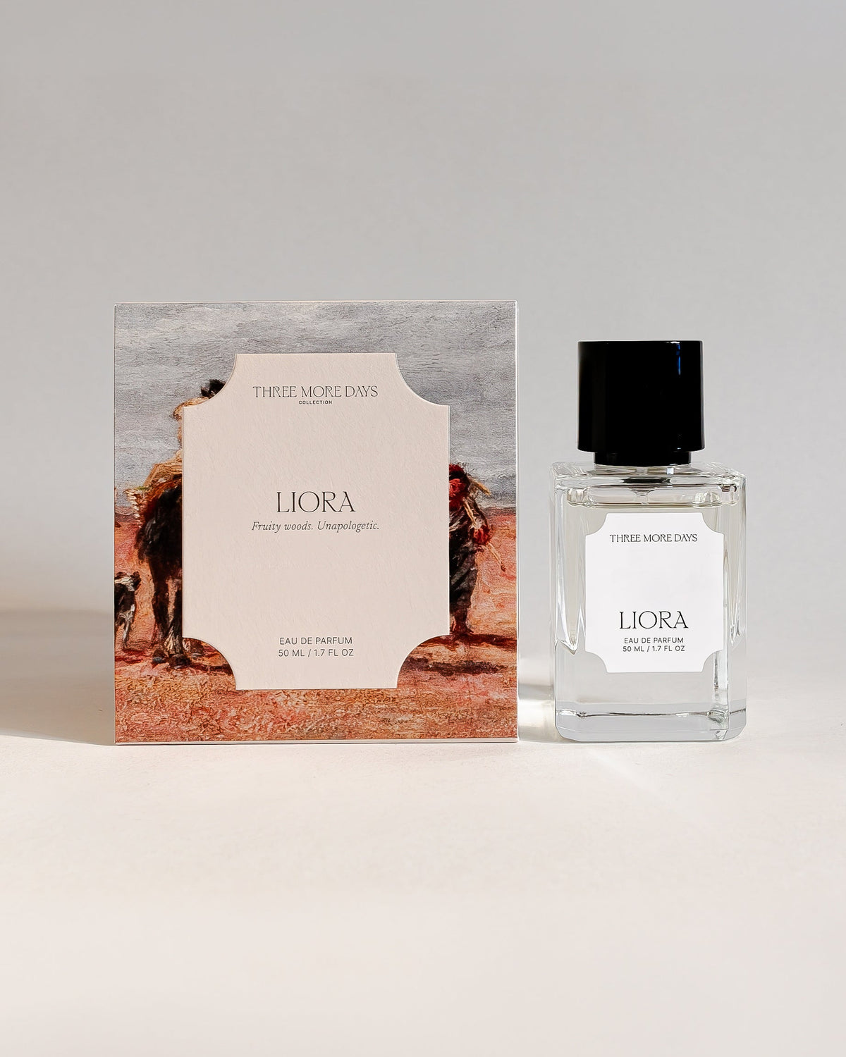 A small clear glass perfume bottle with a black cap stands next to its illustrated box. The packaging features a desert scene with a camel and a camel carrier, with the brand name 'Three Lovers' and product name 'Liora' visible.