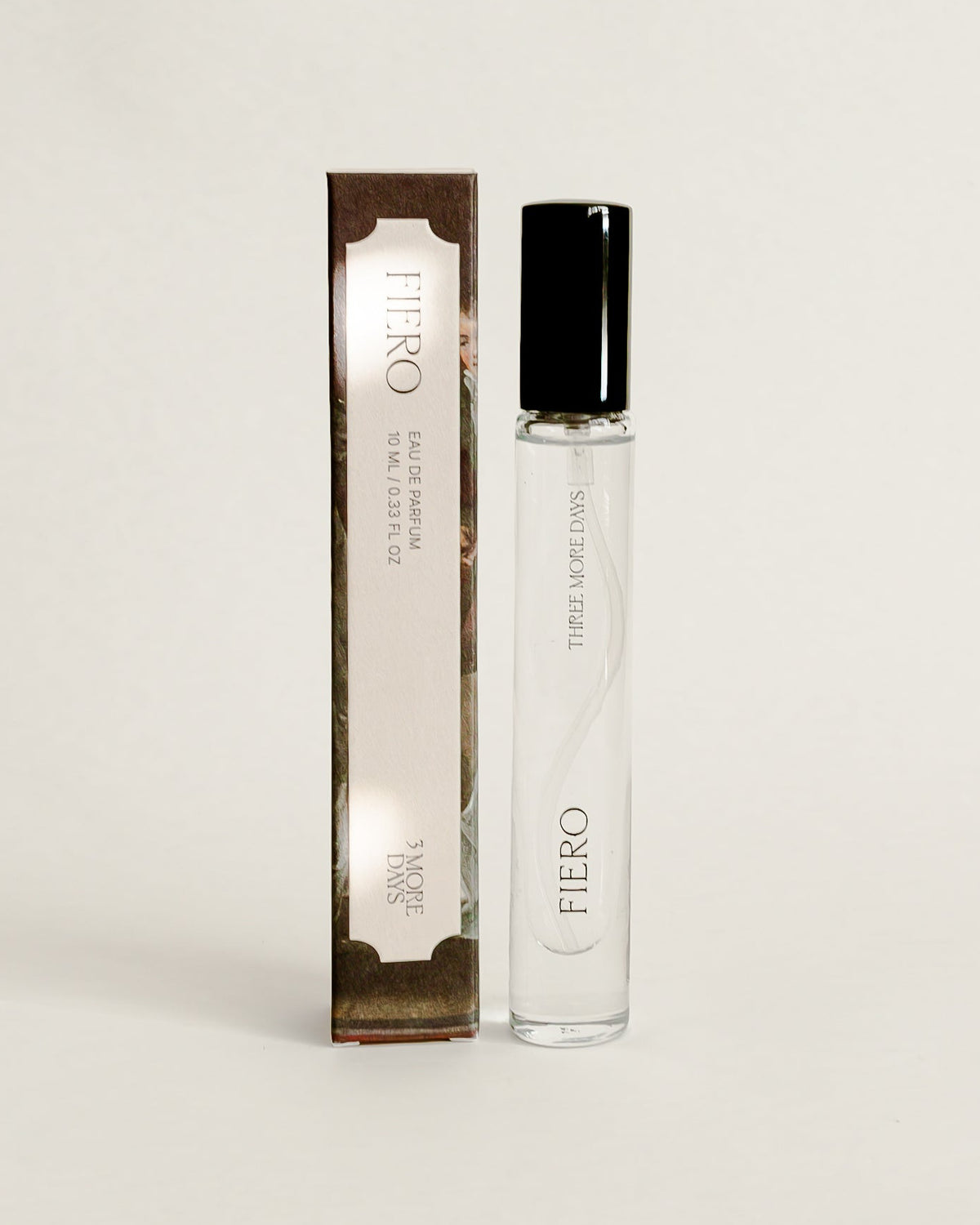 A small cylindrical cosmetic bottle with a black cap stands next to its matching rectangular box on a draped white paper backdrop.