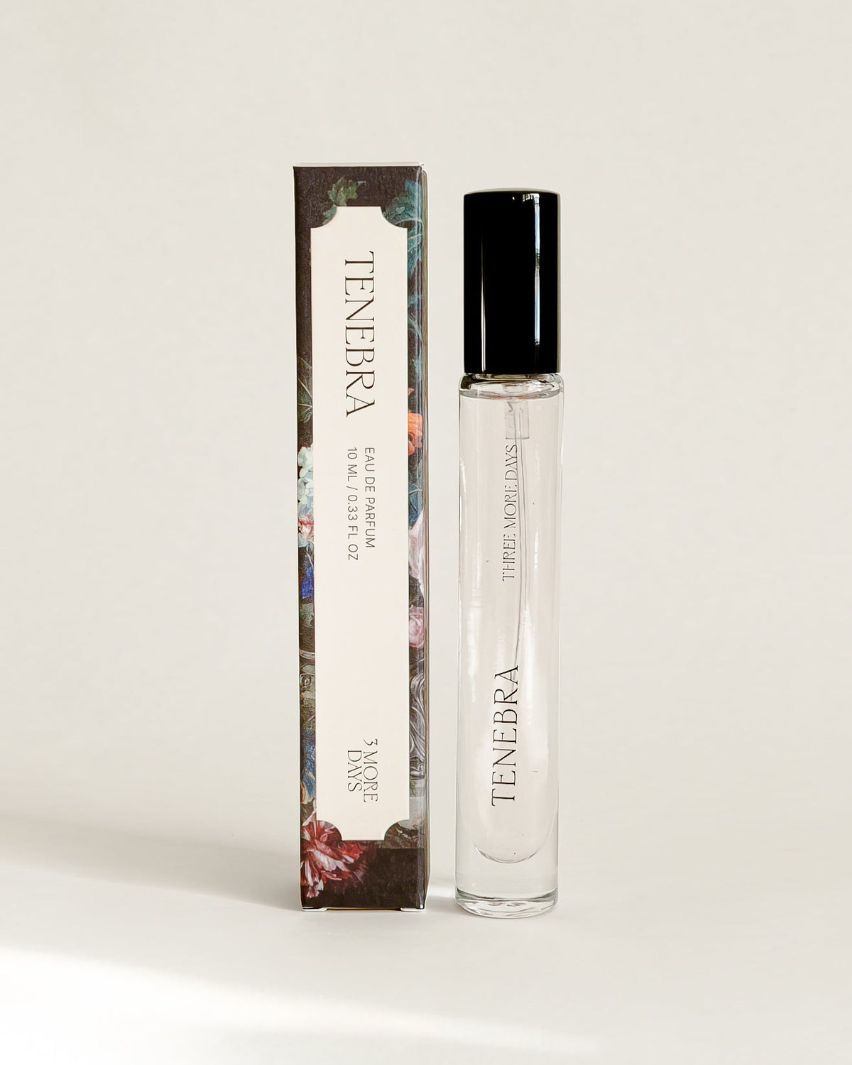 A small cylindrical cosmetic bottle with a black cap stands next to its matching rectangular box on a draped white paper backdrop.