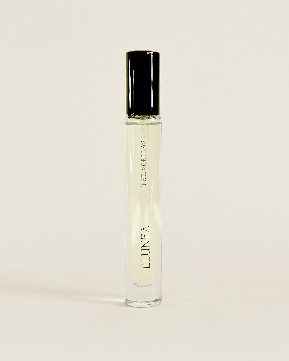 A clear glass perfume roller bottle with a black cap, standing upright on a white surface against a white backdrop.