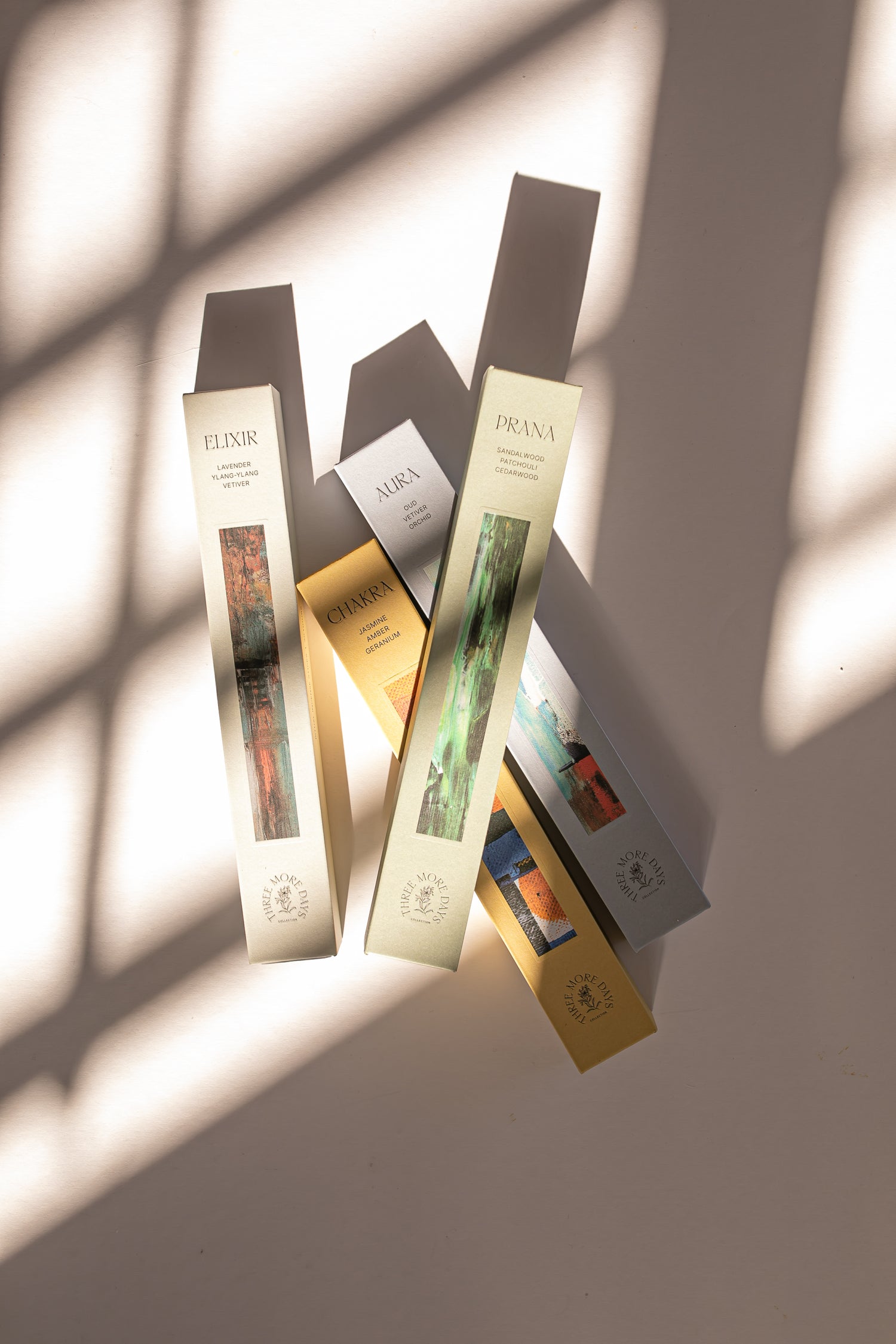 A collection of incense boxes from the Three More Days Collection, featuring Elixir, Aura, Chakra, and Prana. Elegantly designed with natural colors and artistic imagery, displayed under sunlight with stylish shadows.