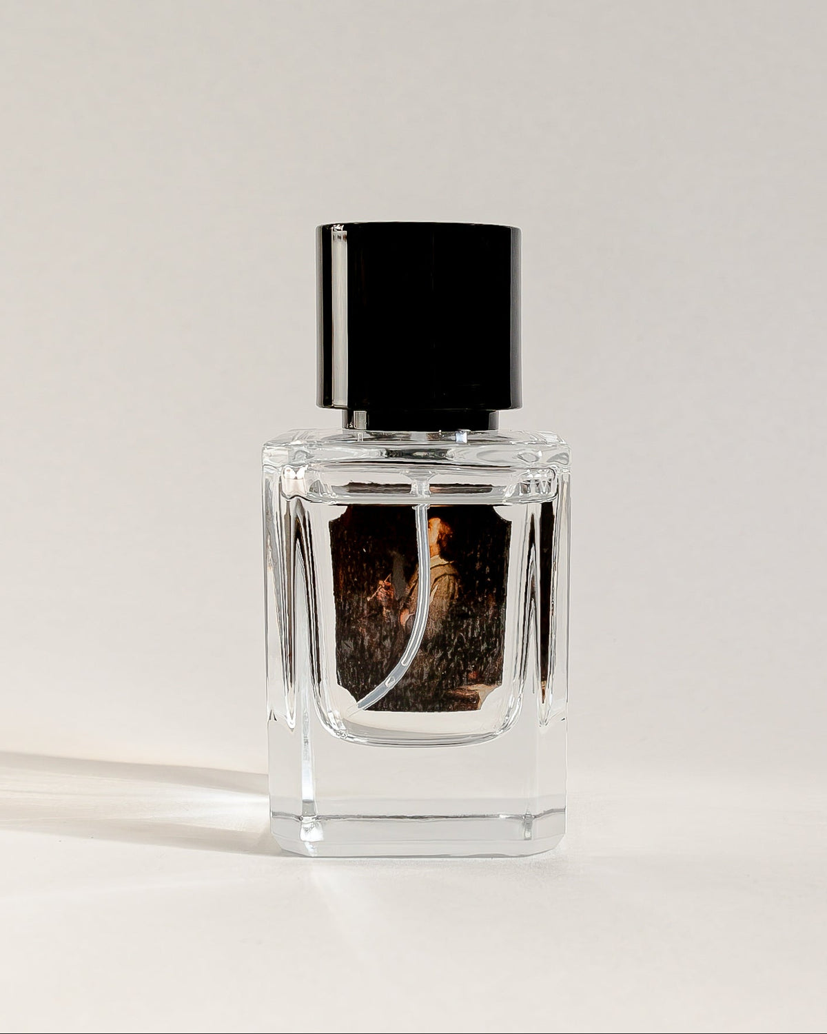 A clear glass perfume bottle with a black cap, containing amber-brown liquid and a dark label, set against a clean white background.