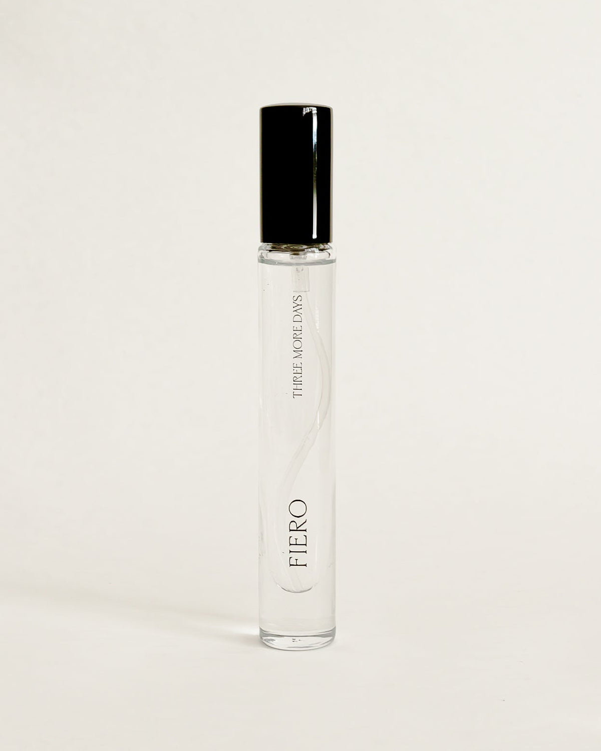 A clear glass perfume roller bottle with a black cap, standing upright on a white surface against a white backdrop.