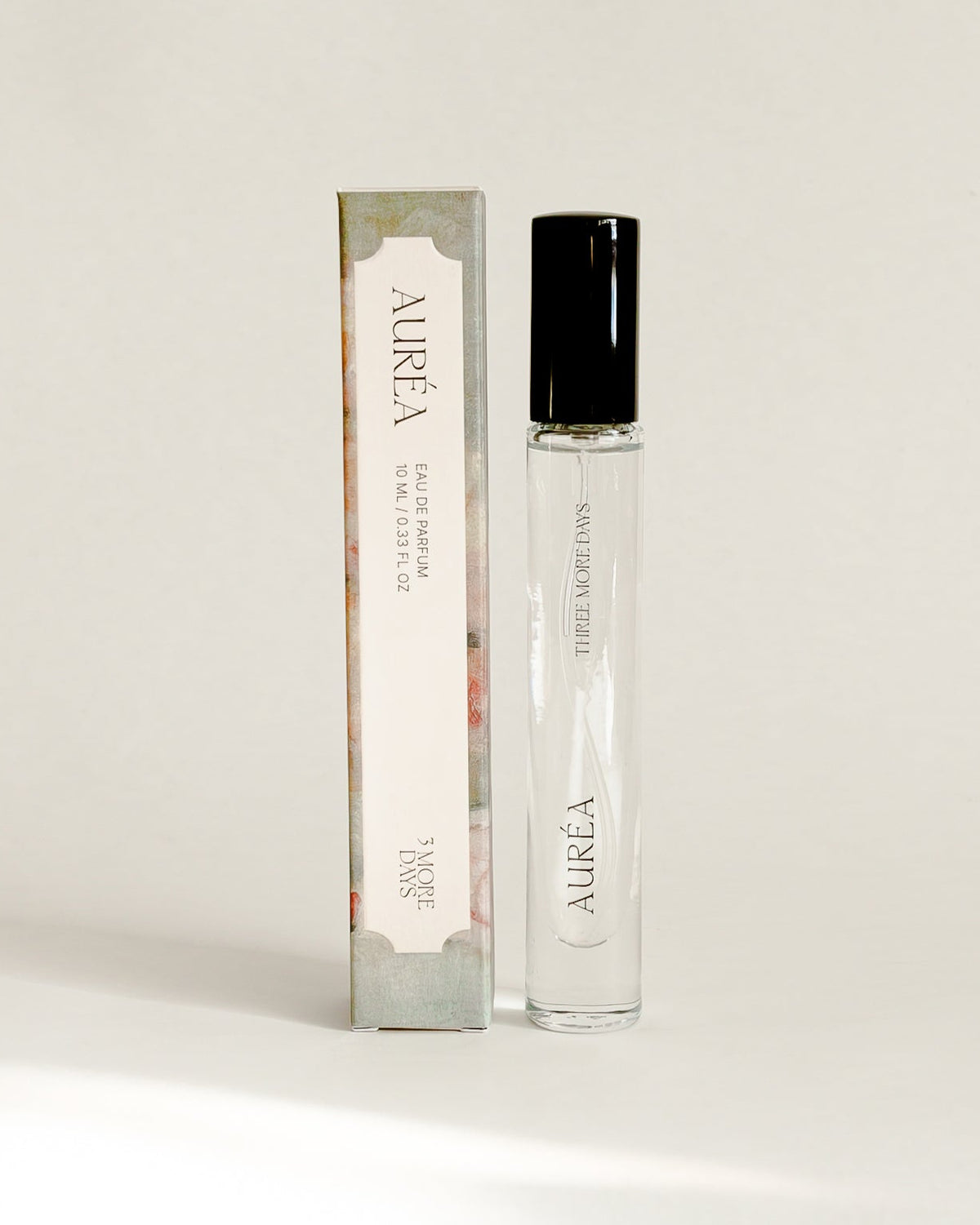 A small cylindrical cosmetic bottle with a black cap stands next to its matching rectangular box on a draped white paper backdrop.