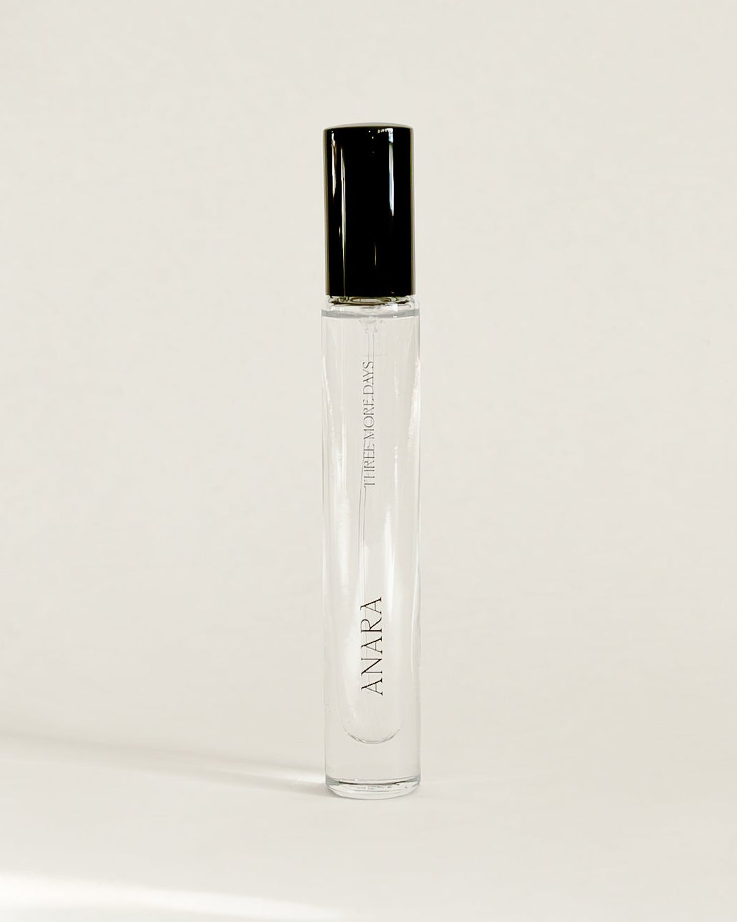 A clear glass perfume roller bottle with a black cap, standing upright on a white surface against a white backdrop. The brand name 'AMARA' is printed vertically on the bottle.
