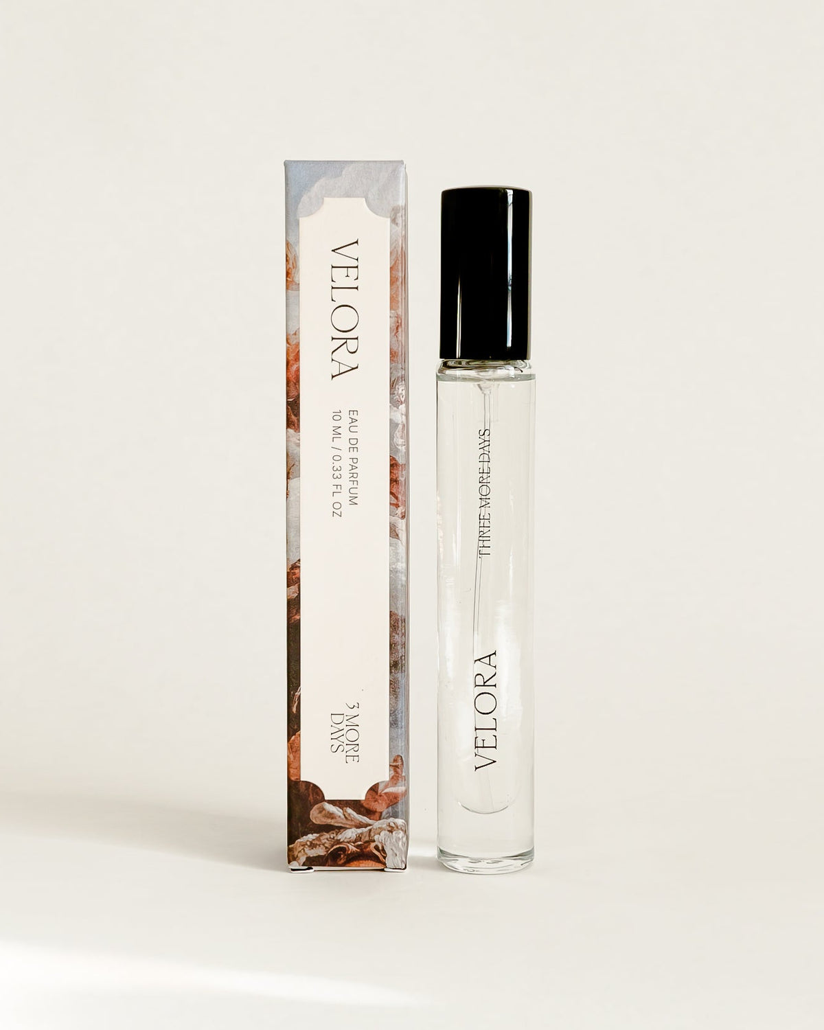 A small cylindrical cosmetic bottle with a black cap stands next to its matching rectangular box on a draped white paper backdrop.