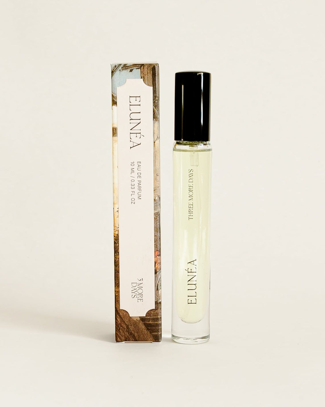 A small cylindrical cosmetic bottle with a black cap stands next to its matching rectangular box on a draped white paper backdrop. 
