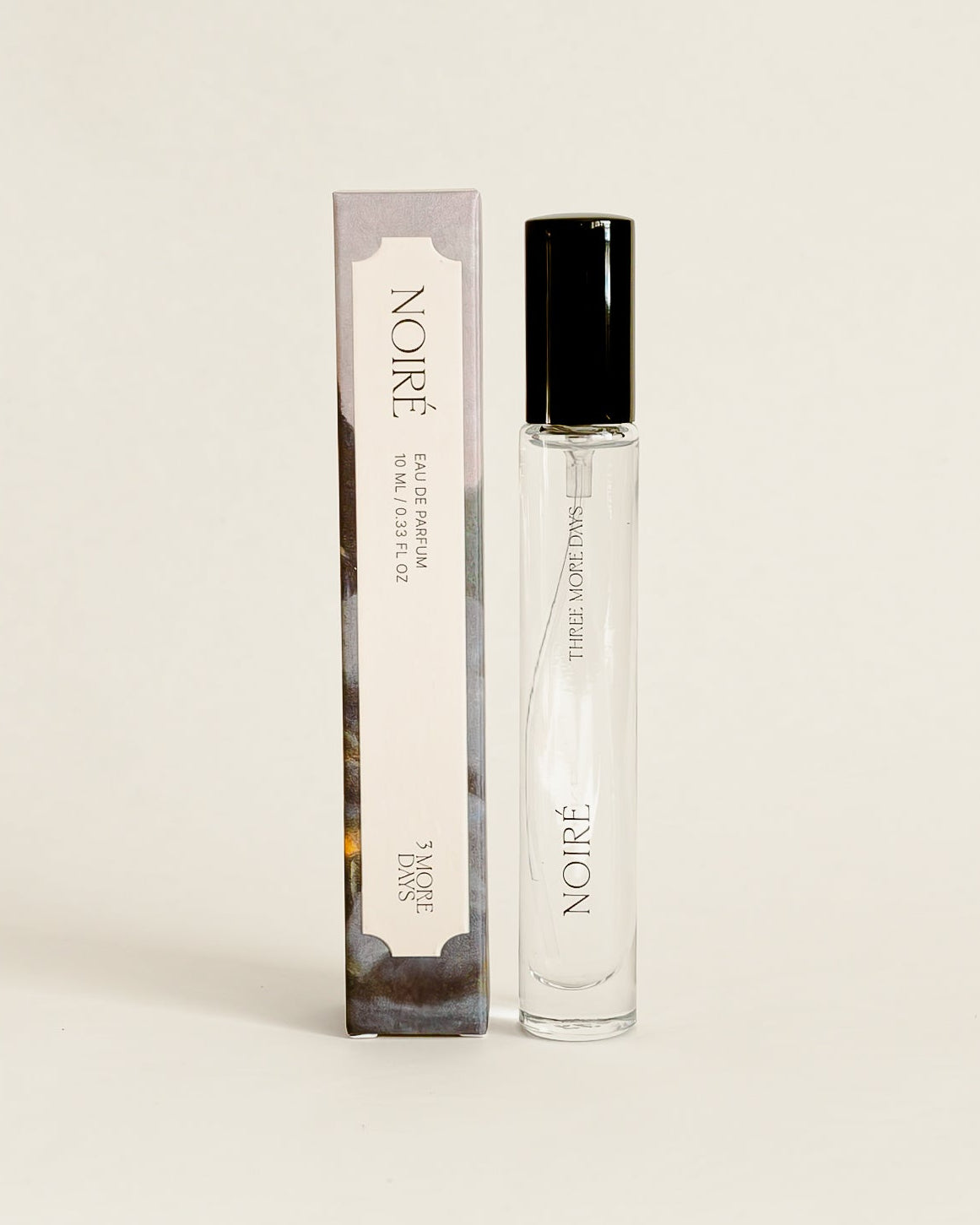 A small cylindrical cosmetic bottle with a black cap stands next to its matching rectangular box on a draped white paper backdrop.