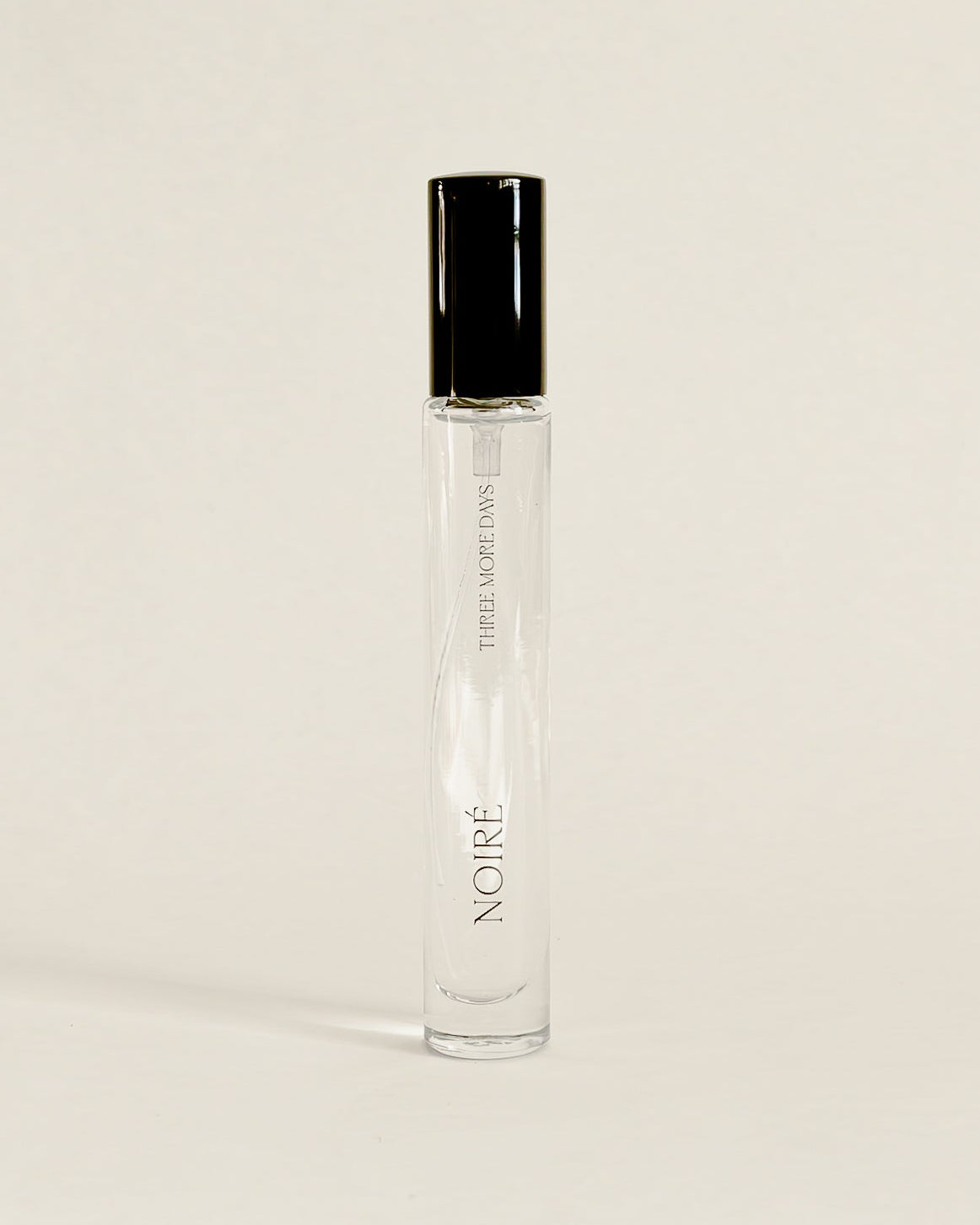 A clear glass perfume roller bottle with a black cap, standing upright on a white surface against a white backdrop.